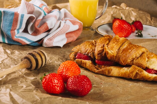 Strawberries near croissant and honey spoon