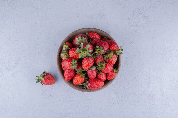 Strawberries piled into a wooden bowl on marble background. High quality photo