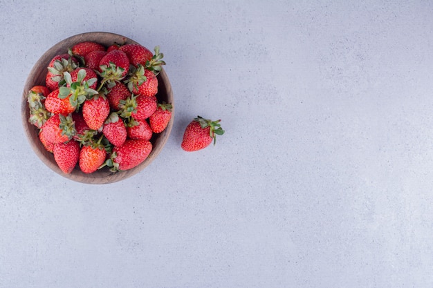 Strawberries piled into a wooden bowl on marble background. High quality photo