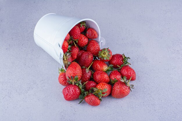 Fragole versando da un piccolo secchio su sfondo marmo. foto di alta qualità