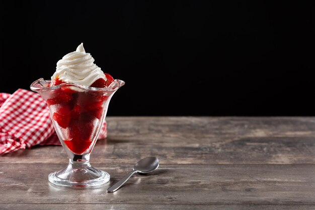 Strawberries and whipped cream in ice cream glass on wooden table