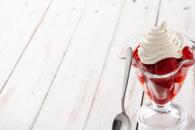 Strawberries and whipped cream in ice cream glass on wooden table