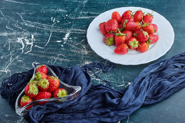 Strawberries in a white plate and inside glass cup. 