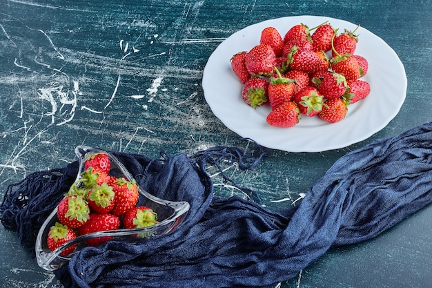 Strawberries in a white plate and inside glass cup. 