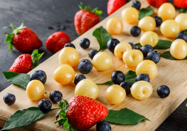 Strawberries with blueberries, cherries, leaves high angle view on grey and cutting board