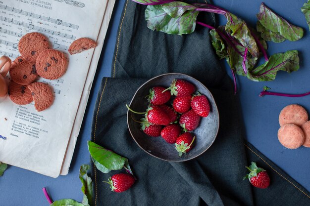 딸기 그릇 및 쿠키, 시금치 잎, balck 매트에 책.