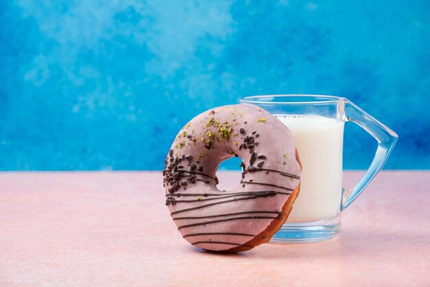 Strawberry donut with decorations and a glass of milk on pink table. 