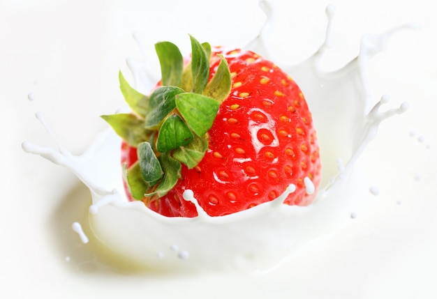 Strawberry falling into milk