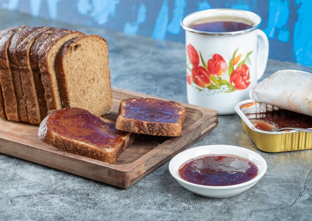 Strawberry jam with slice of brown bread and cup of tea.