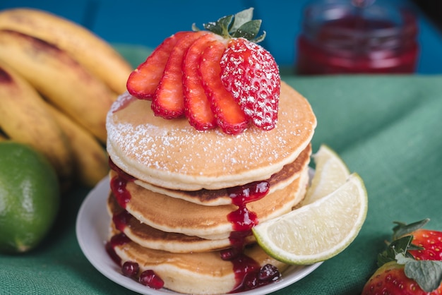 Strawberry slices on stacked of pancake served on plate with lime slice