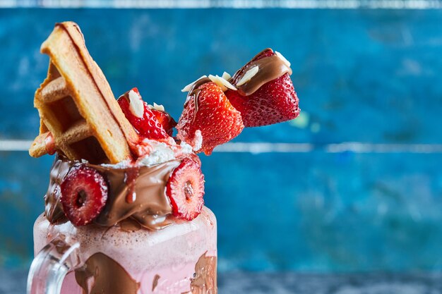 Strawberry smoothie with tiny waffle, chocolate and slices of strawberries in the dark blue surface 