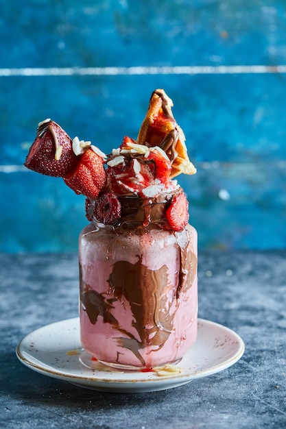 Strawberry smoothie with tiny waffle, chocolate and slices of strawberries on the white plate in the dark blue surface