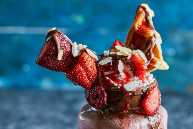 Strawberry smoothie with tiny waffle, chocolate and slices of strawberries on the white plate in the dark blue surface