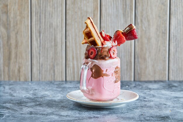 Strawberry smoothie with tiny waffle, chocolate and slices of strawberries on the white plate in the dark blue surface