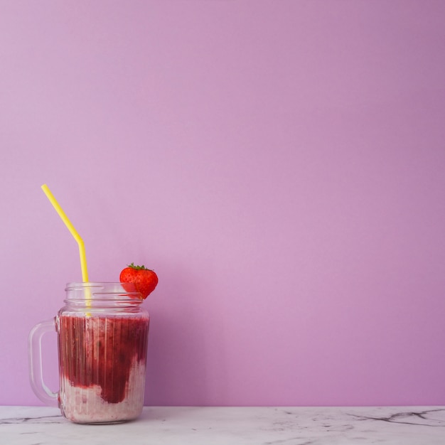 Strawberry smoothie with yellow straw in jar against pink background