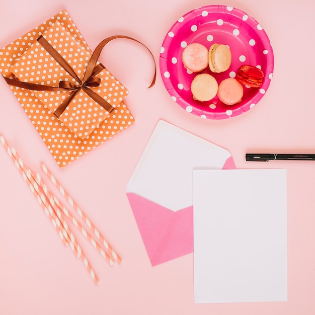 Straws and paper sheet near present and macaroons