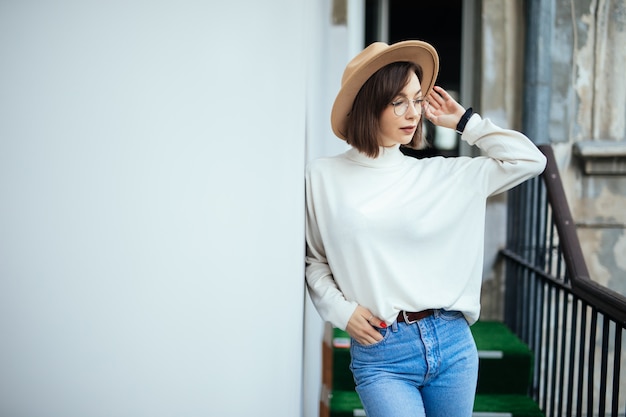 Street fashion interested woman wearing hat, blue jeans, wide hat and transperent glasses on balcony