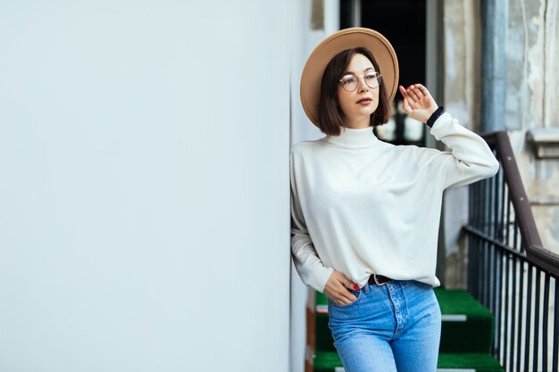 Street fashion interested woman wearing hat, blue jeans, wide hat and transperent glasses on balcony