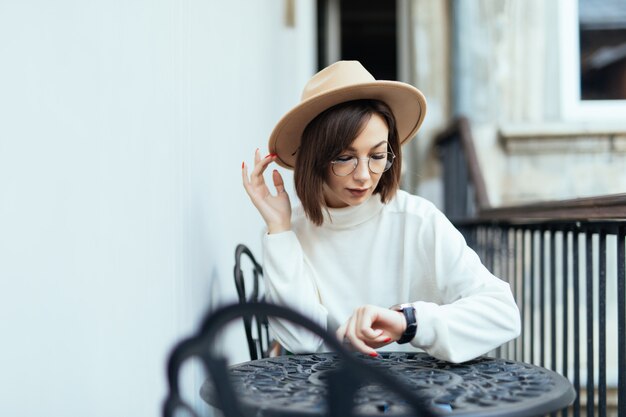 Street fashion woman with modern manicure and transperent glasses sitting at the table