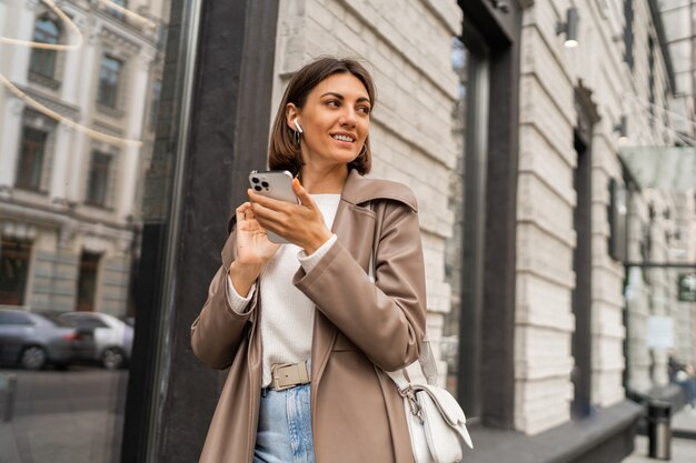 屋外でポーズをとる革のコートでスタイリッシュなヨーロッパのビジネスブルネットの女性のストリートライフスタイルの肖像画