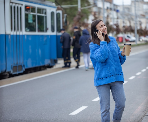 Street portrait of a young woman talking on the phone in the city near the roadway.