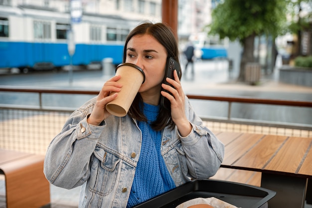 커피를 마시고, 전화로 이야기하고, 누군가를 기다리는 젊은 여성의 거리 초상화.