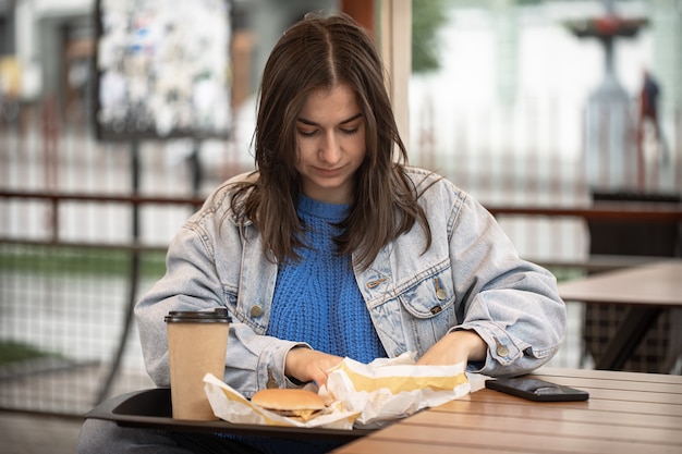 Street portrait of a young woman with fast food on the summer terrace of a cafe