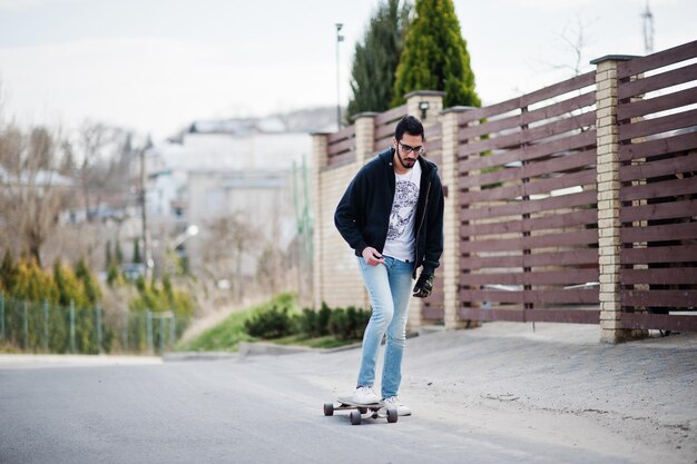 Street style arab man in eyeglasses with longboard longboarding down the road