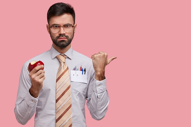 Бесплатное фото Серьезный босс стрэн носит очки с толстыми линзами, ест вкусное яблоко, одет в строгую рубашку