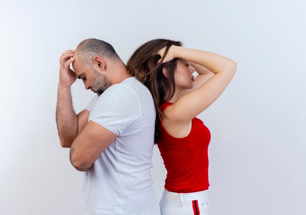 Stressed adult couple standing back to back both putting hand on head isolated on white wall with copy space