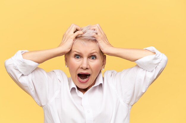 Stressed angry retired woman shouting and pulling hair off having furious desperate look, suffering from headache, expressing negative reaction. Stress, despair, nervous wreck and breakdown