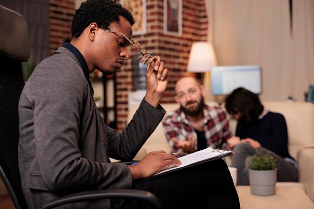 Stressed counselor taking notes on paper at couple therapy session with married partners, having relationship conflict and difficulties. Trying to solve problems with psychology advice.