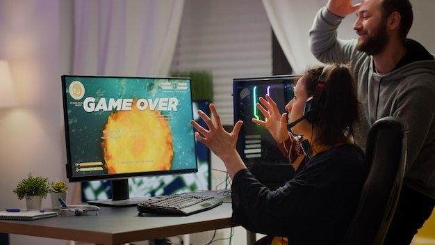 Foto gratuita coppia di giocatori stressati che perdono il videogioco sparatutto spaziale giocando su un potente computer rgb durante lo streaming della competizione online. pro cyber donna con auricolare che si esibisce da casa durante il torneo virtuale