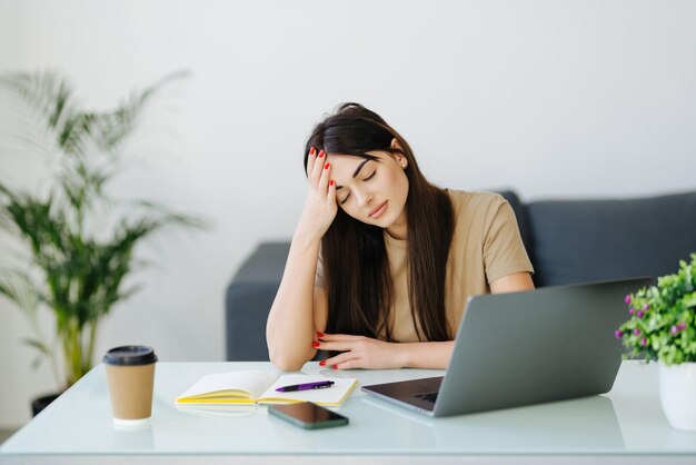 ラップトップを見てストレスを感じている欲求不満の若い女性の学生が悪い電子メールを読んでいるインターネットのニュースは、オンラインでの勉強にうんざりしていると感じています。