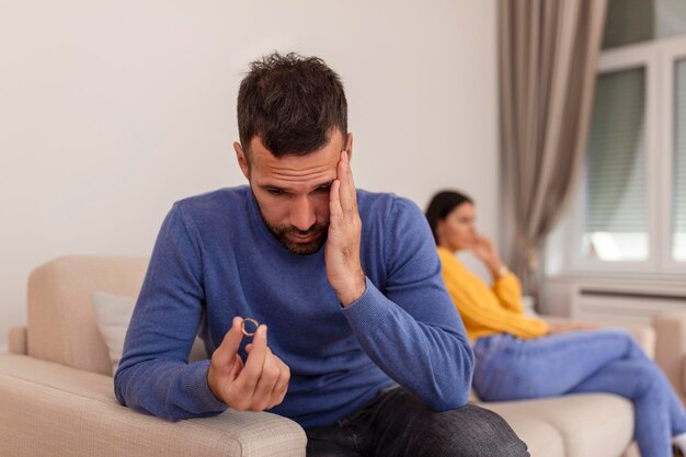 Stressed man holding her wedding ring worried about breakup or divorce avoid talking with wife after fight anxious couple ignore each other Frustrated sad husband taking off the wedding ring