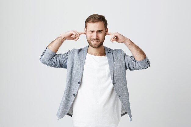 Stressed man with beard shut ears with fingers