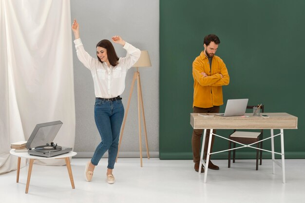 Stressed man working on laptop and woman dancing