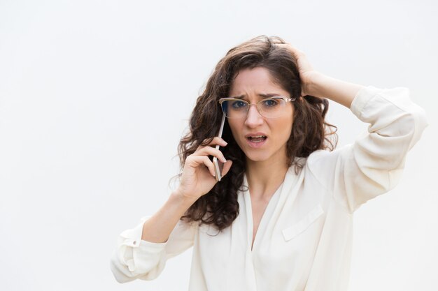 Stressed puzzled woman in glasses talking on mobile phone