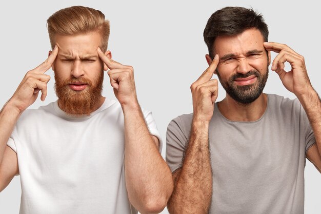 Stressed two unshaven young man friends keep fore fingers on temples, have depressed expressions