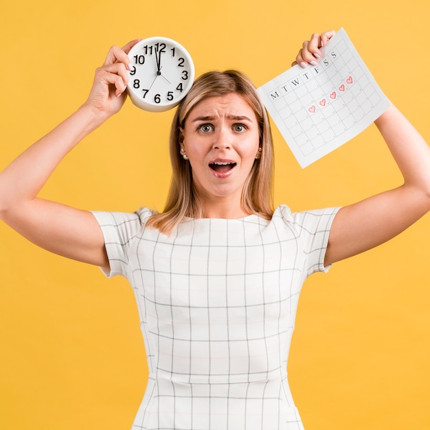 Stressed woman holding clock and period calendar