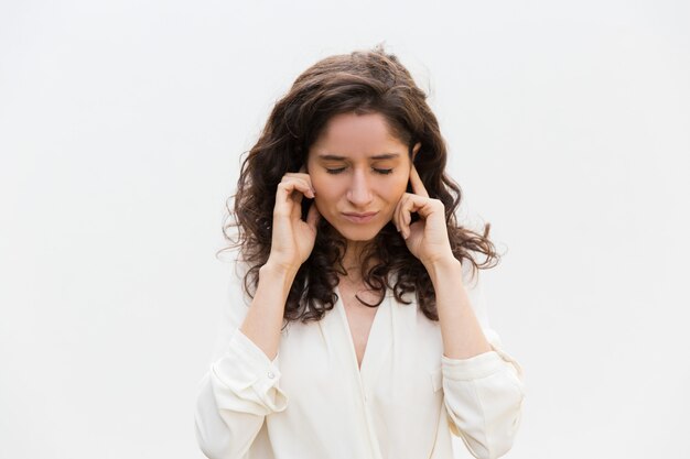 Stressed woman with closed eyes plugging ears with fingers