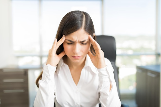 Stressed young female manager with headache touching temples in office