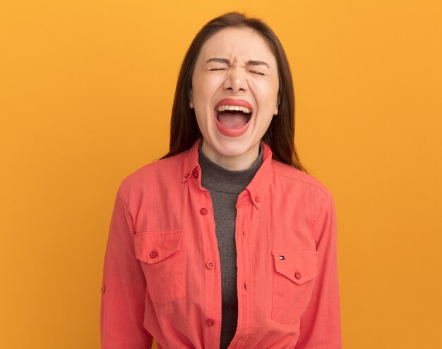 Stressed young pretty woman screaming with closed eyes isolated on orange wall