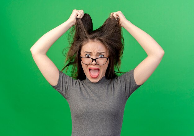 Free photo stressed young pretty woman wearing glasses pulling her hair isolated on green background