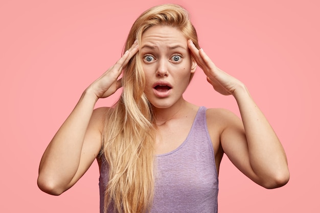 Stressed young woman keeps hands on temples, notices or remembers something terrific, has scared expression