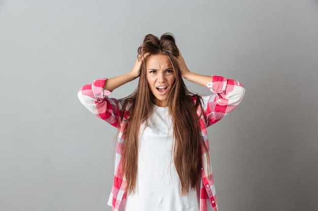 Foto gratuita giovane donna sollecitata nella testa commovente di rabbia e che grida con la bocca aperta in camicia a quadretti