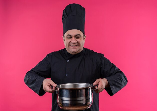 Stresses middle-aged male cook in chef uniform holding heavy saucepan