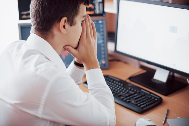 Stressful day at the office. Young businessman holding hands on his face while sitting at the desk in creative office. Stock Exchange Trading Forex Finance Graphic Concept