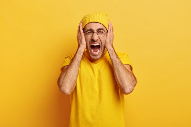 Stressful depressed man screams out loudly, covers ears, being fed up with troubles