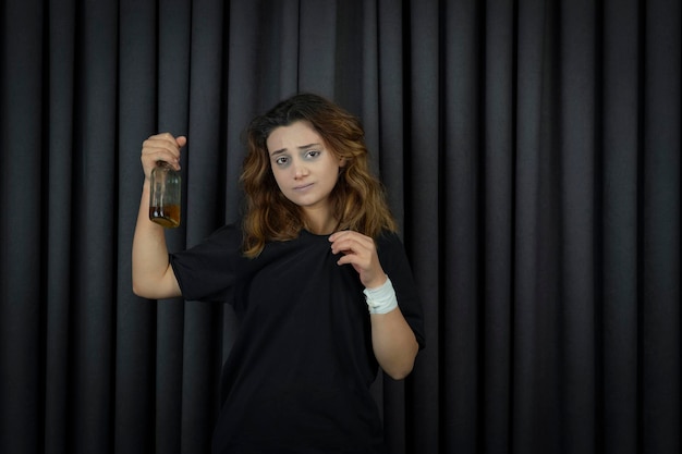 Стрессовая молодая девушка держит бутылку с алкоголем и смотрит в камеру. Фото высокого качества